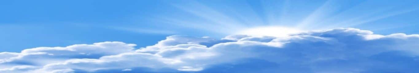 Sun shinning in blue sky through white puffy clouds.