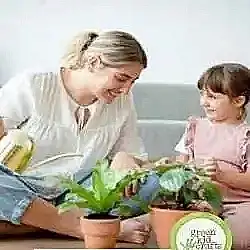 Mother and daughter setting on floor with mom showing daughter how to water two flower pots which is one of the 6 tips for indoor gardening with kids.