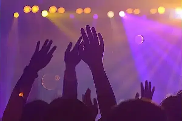 Hands raised in worship under vibrant stage lights.